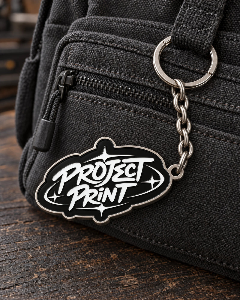 Project Print custom metal enamel keyring design in matt nickel, attached to a charcoal canvas bag.
