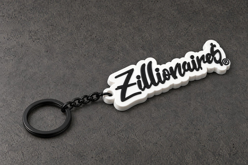 zillionaire white script keyring on a charcoal studio surface — Projectprint