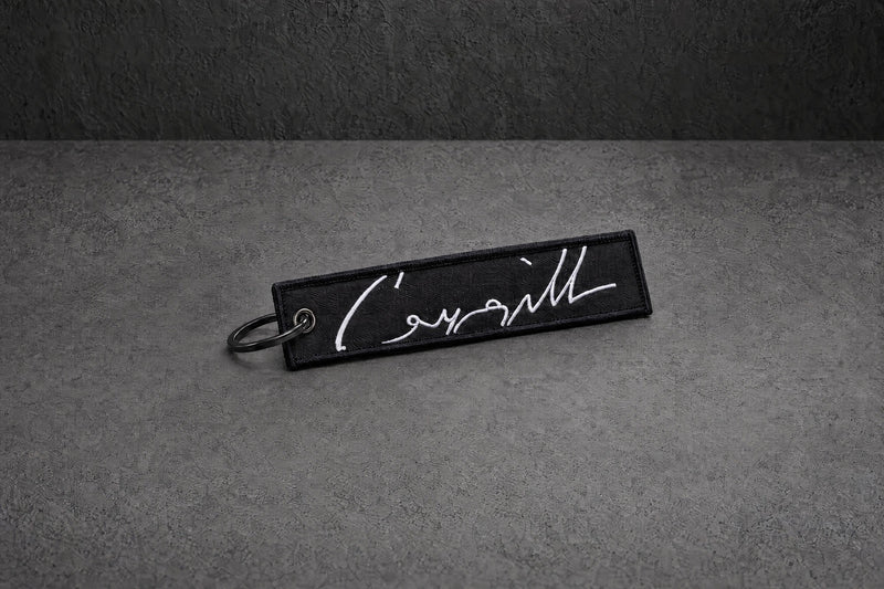 white signature stitched keyring on a charcoal studio surface — Projectprint