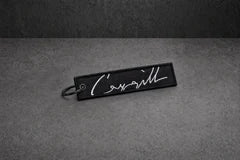 white signature stitched keyring on a charcoal studio surface — Projectprint